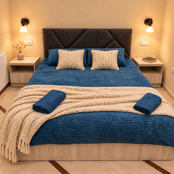 A bed with a dark headboard, two bedside tables, and a wall-mounted lamp.