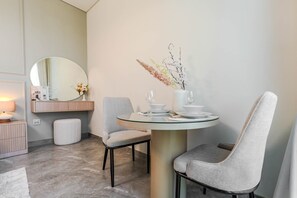 A modern dining area with a round glass table, two grey upholstered chairs, a white vase with dried flowers, and a mirror above the table. - HAVN - High floor Studio, Burj Khalifa View (Dubai)