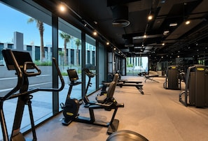 A gym with exercise equipment and large windows overlooking a cityscape. - HAVN - High floor Studio, Burj Khalifa View (Dubai)