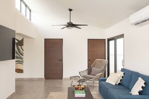 Uma sala de estar moderna com ventilador de teto, um sofá azul, uma poltrona de vime e uma mesa de centro com livros.