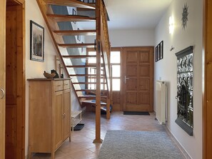 A wooden staircase leading to a second floor, a wooden cabinet with drawers, a radiator, and a door with decorative metalwork.