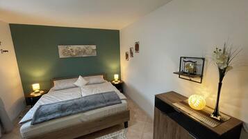 Une chambre à coucher comprenant un lit, des lampes de chevet, une table de chevet, un élément décoratif mural, une petite étagère avec une lampe et un vase avec des fleurs.