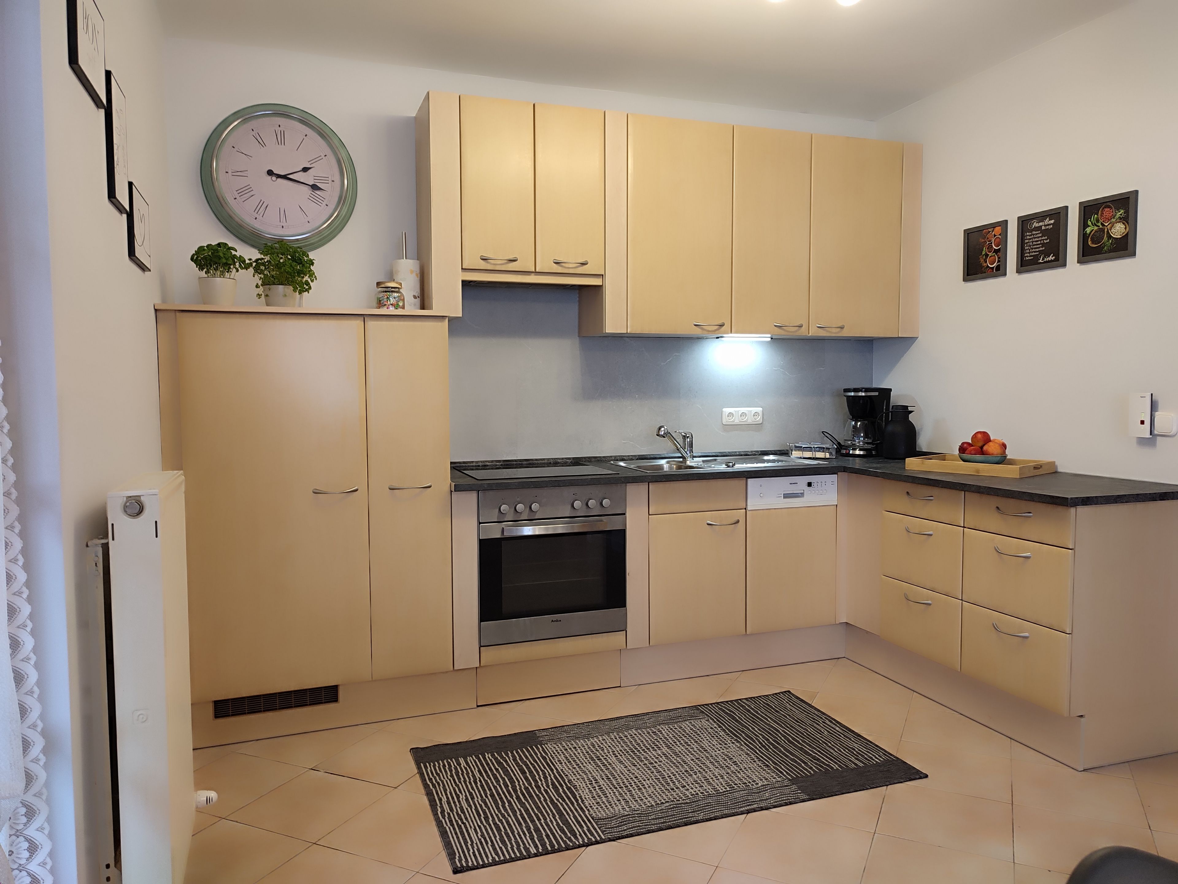 Une cuisine moderne avec des meubles de couleur beige, une cuisinière en acier inoxydable, un lave-vaisselle et une horloge murale.