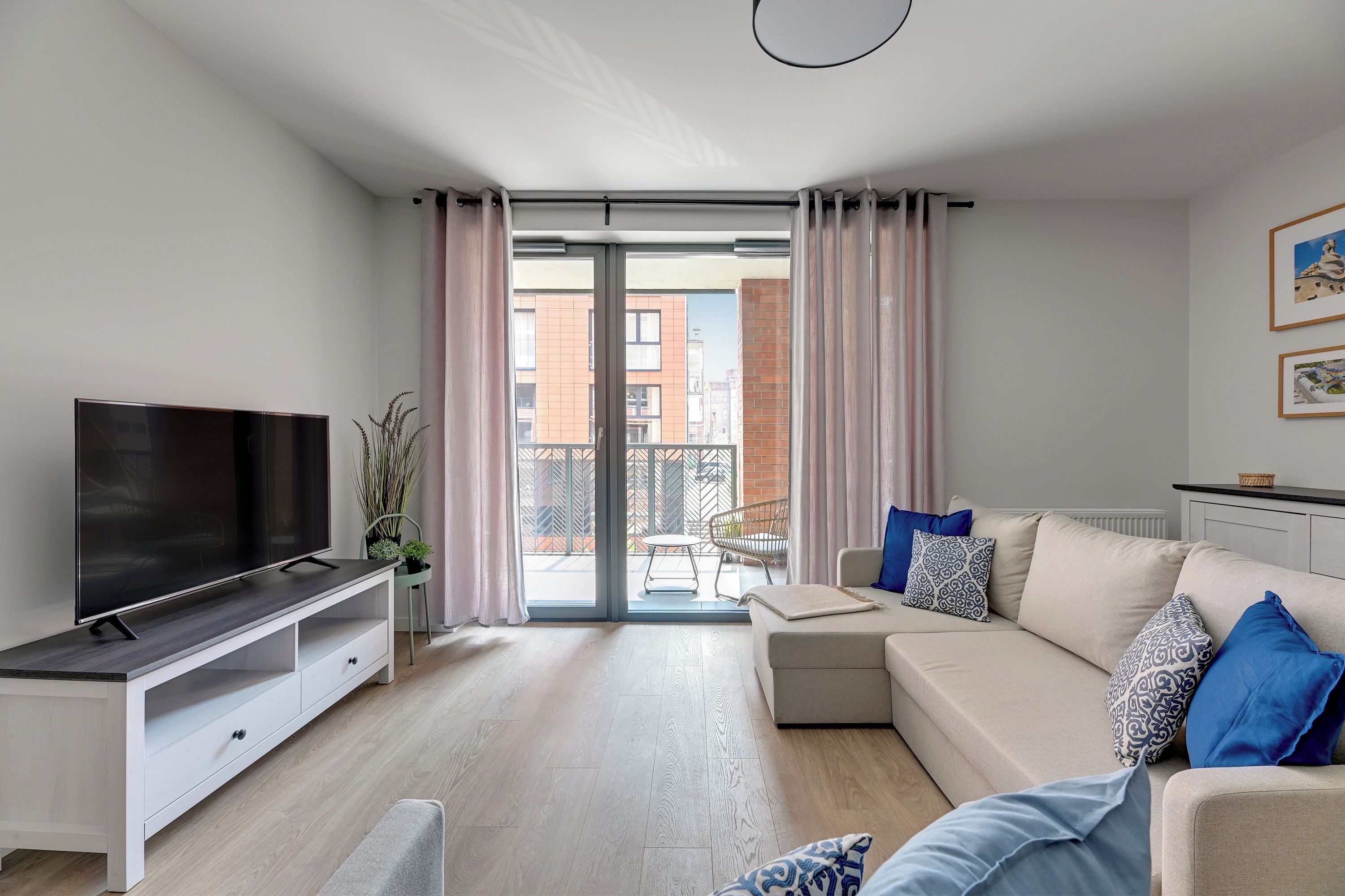 Ett modernt vardagsrum med en platt-TV, en soffgrupp, en matplats med en stol och utsikt över stadsbilden genom balkongdörrarna.
