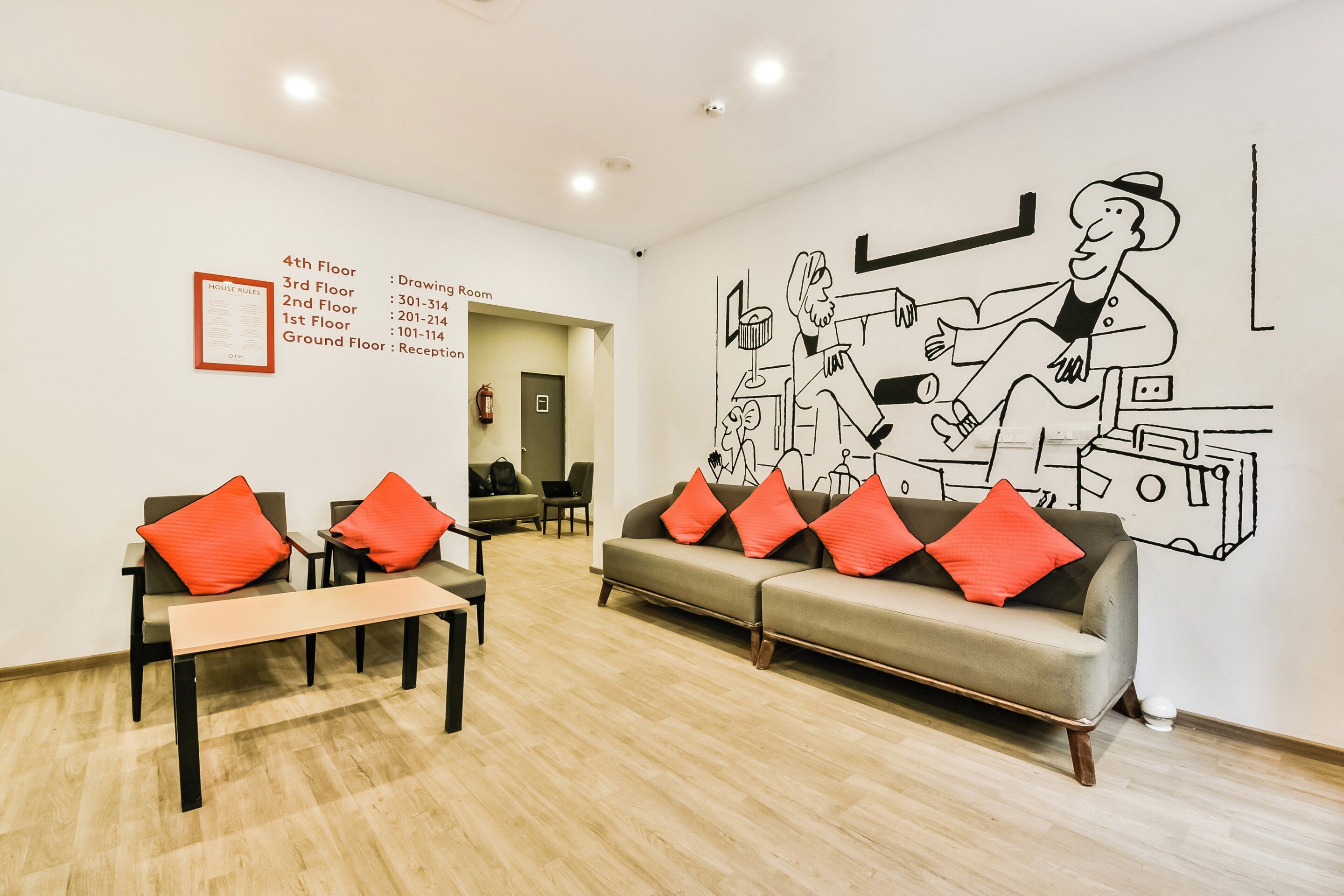 Um saguão de hotel com uma mesa de recepção, um sofá com almofadas vermelhas e um mural na parede.