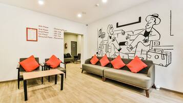 Um saguão de hotel com uma mesa de recepção, um sofá com almofadas vermelhas e um mural na parede.