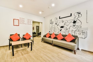 Un hall de hotel con una recepción, un sofá con cojines rojos y un mural en la pared.