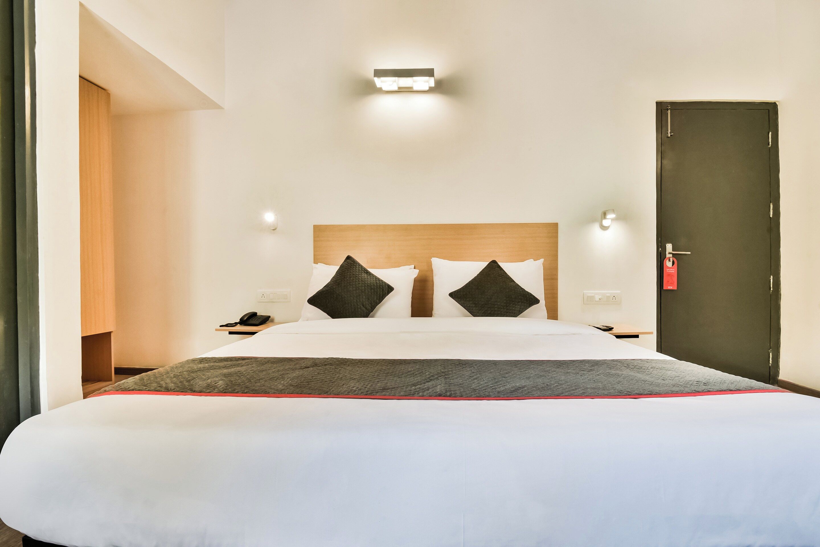 Una habitación de hotel con una cama grande, una mesita de noche, un teléfono y una puerta.