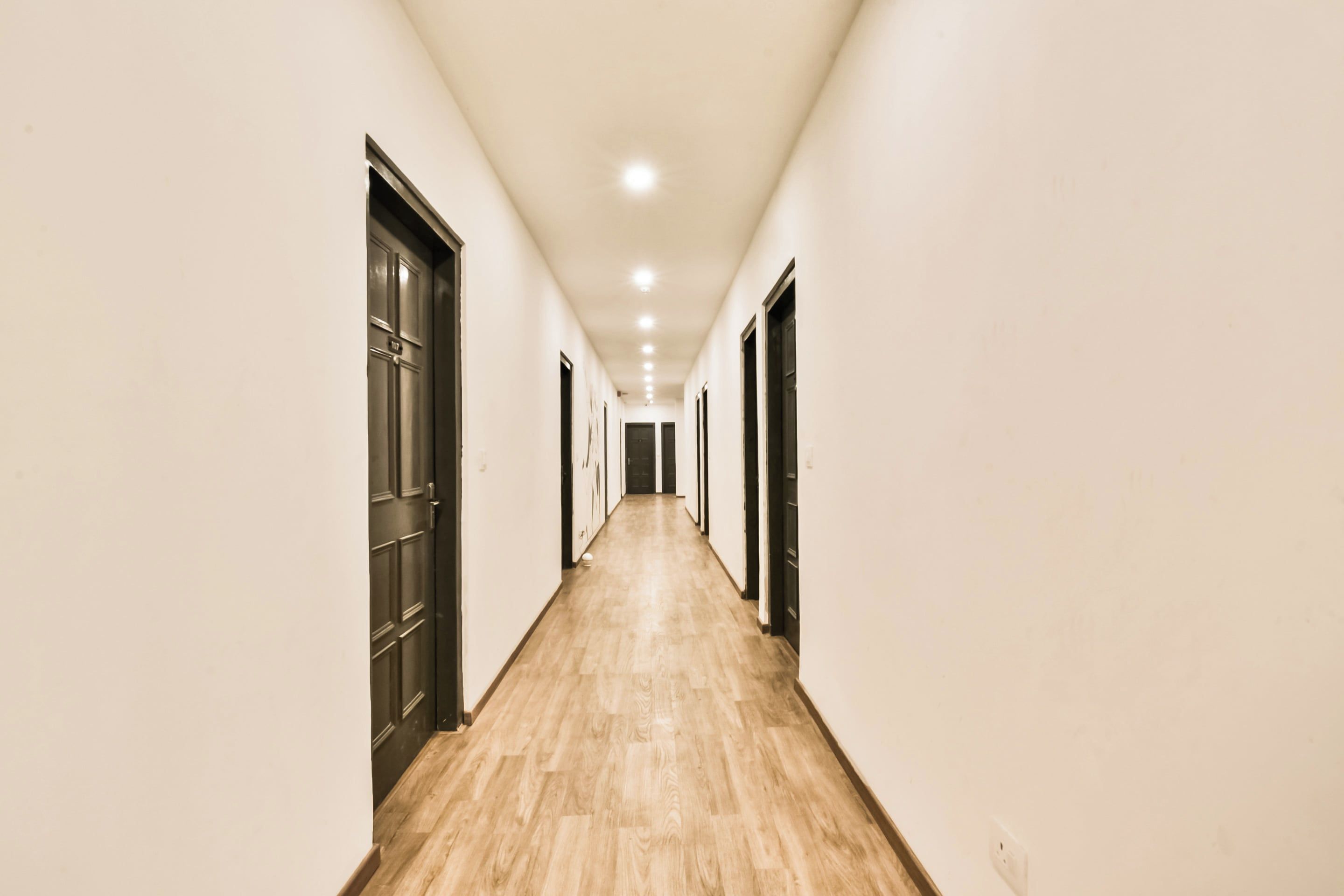 Um corredor comprido e estreito com piso de madeira e portas em ambos os lados.