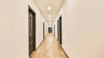 Um corredor comprido e estreito com piso de madeira e portas em ambos os lados.