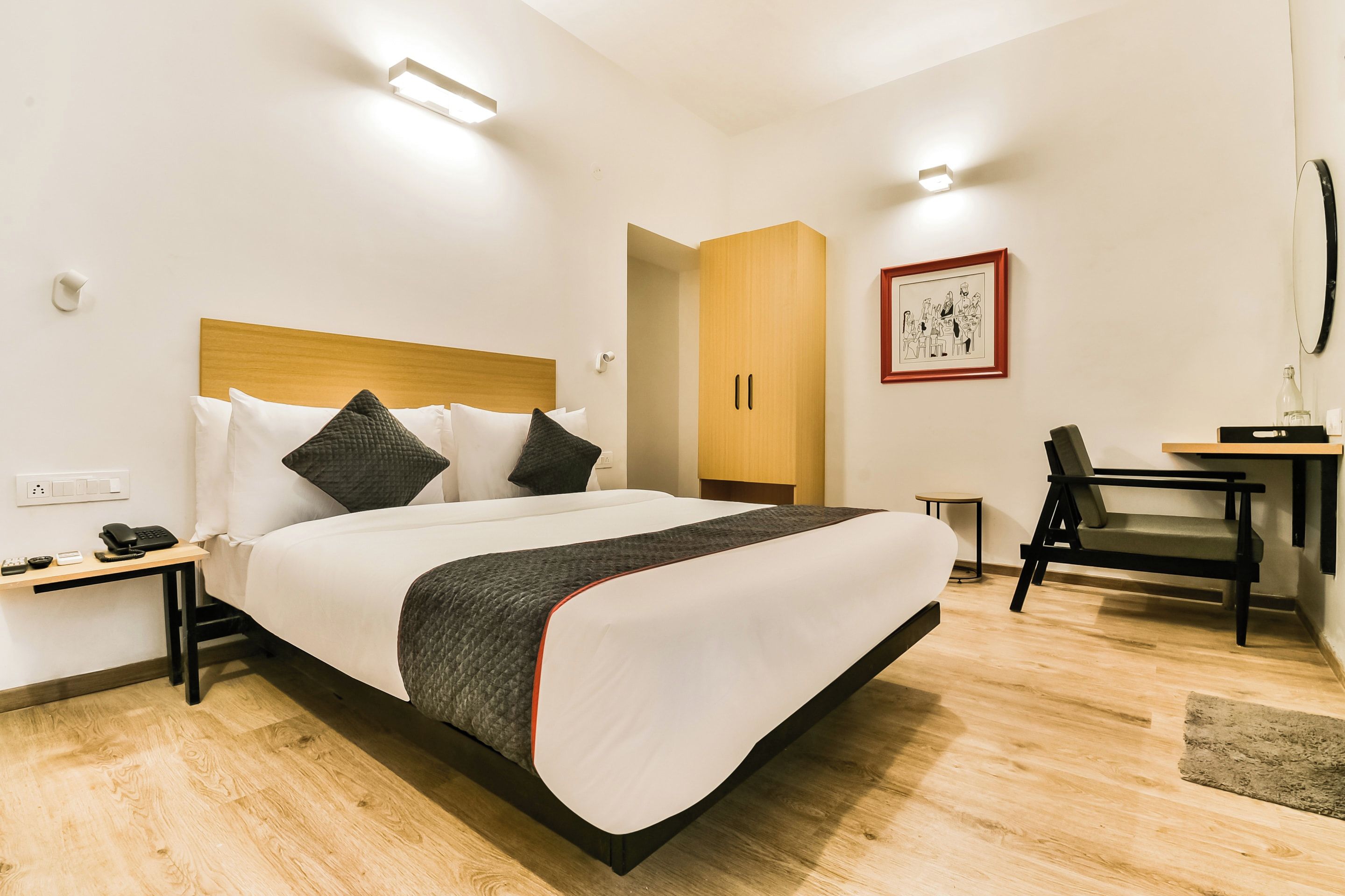 Quarto de hotel com cama, mesa de cabeceira, escrivaninha, cadeira e um quadro na parede.