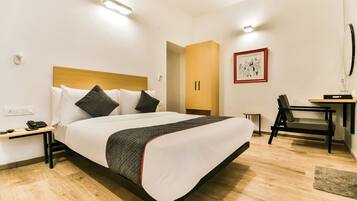 Quarto de hotel com cama, mesa de cabeceira, escrivaninha, cadeira e um quadro na parede.