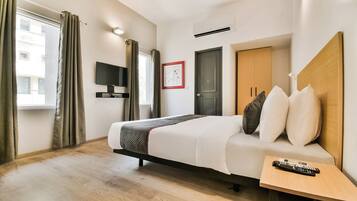 Habitación de hotel con una cama, televisión, puerta y ventana con cortinas.