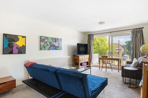 A modern living room with a blue sofa, a TV, and a dining area with a table and chairs. - GuestReady - Charming North London Retreat (London)