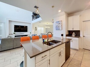 A modern kitchen with a central island, white cabinetry, and a dining area with orange chairs. - Sunshine Retreat: Private Pool and Spa! (Davenport)