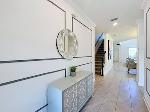 A hallway with a geometric-patterned console table, a round mirror, and a staircase leading to another room. - Sunshine Retreat: Private Pool and Spa! (Davenport)