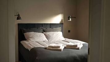 Una cama bien hecha con almohadas y toallas dobladas, dos lámparas de pared y un cabecero.