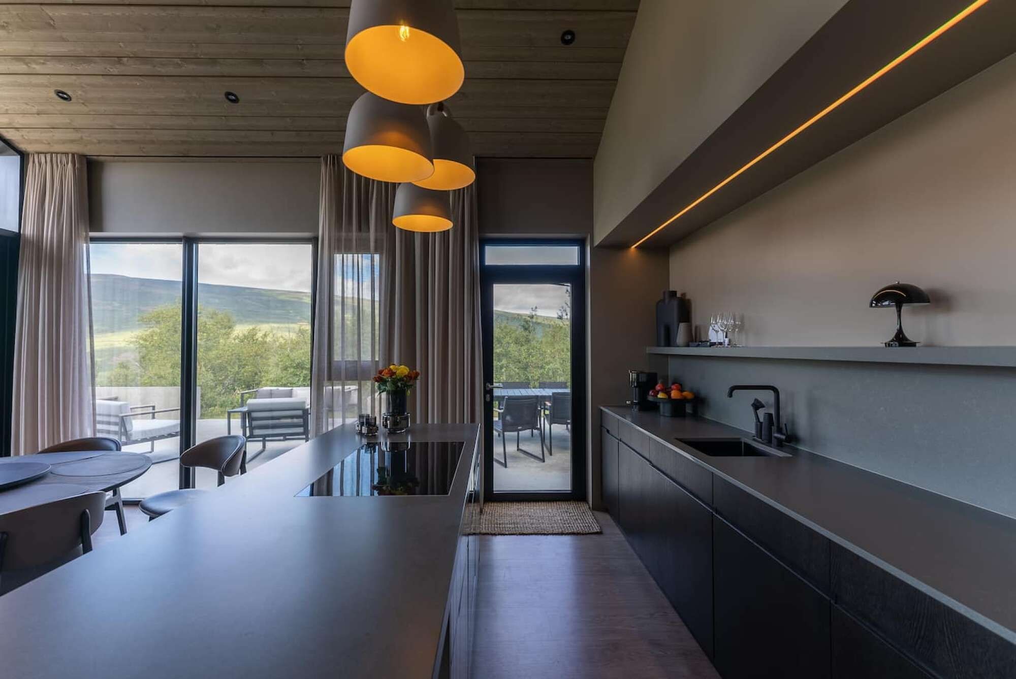 Een moderne keuken met een groot eiland, hanglampen en uitzicht op de omgeving.