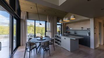 Een moderne keuken met een centraal eiland, een eetgedeelte met stoelen en grote ramen met uitzicht op de omgeving.