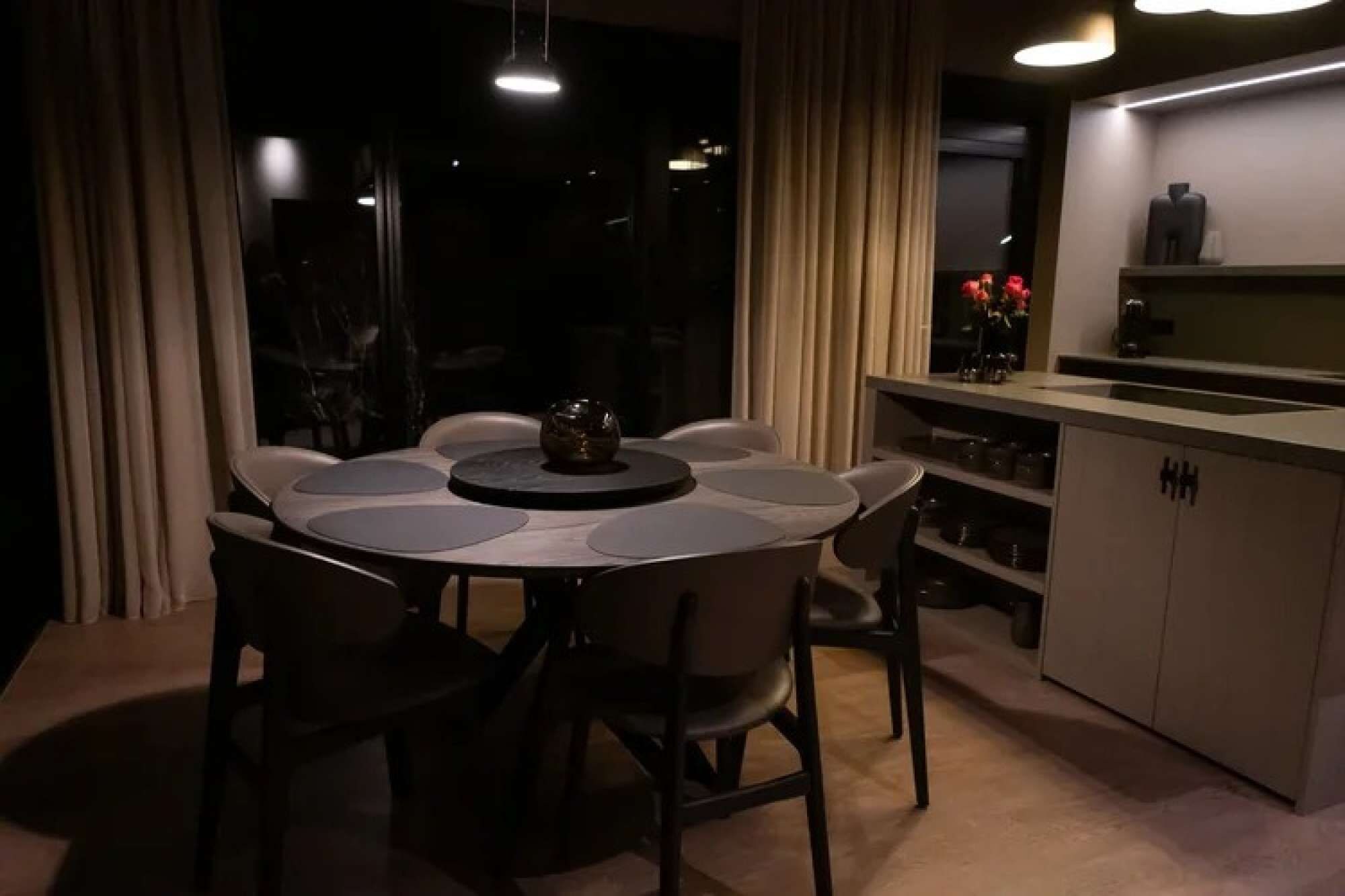 Un coin repas avec une table ronde et des chaises, un espace cuisine avec des placards et un comptoir, et une vue par une fenêtre avec des rideaux.