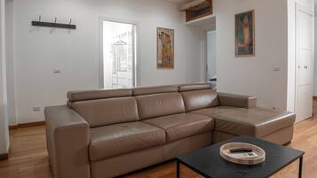 Un salon moderne avec un canapé d’angle beige, une table basse noire, un plancher en bois et des murs blancs.