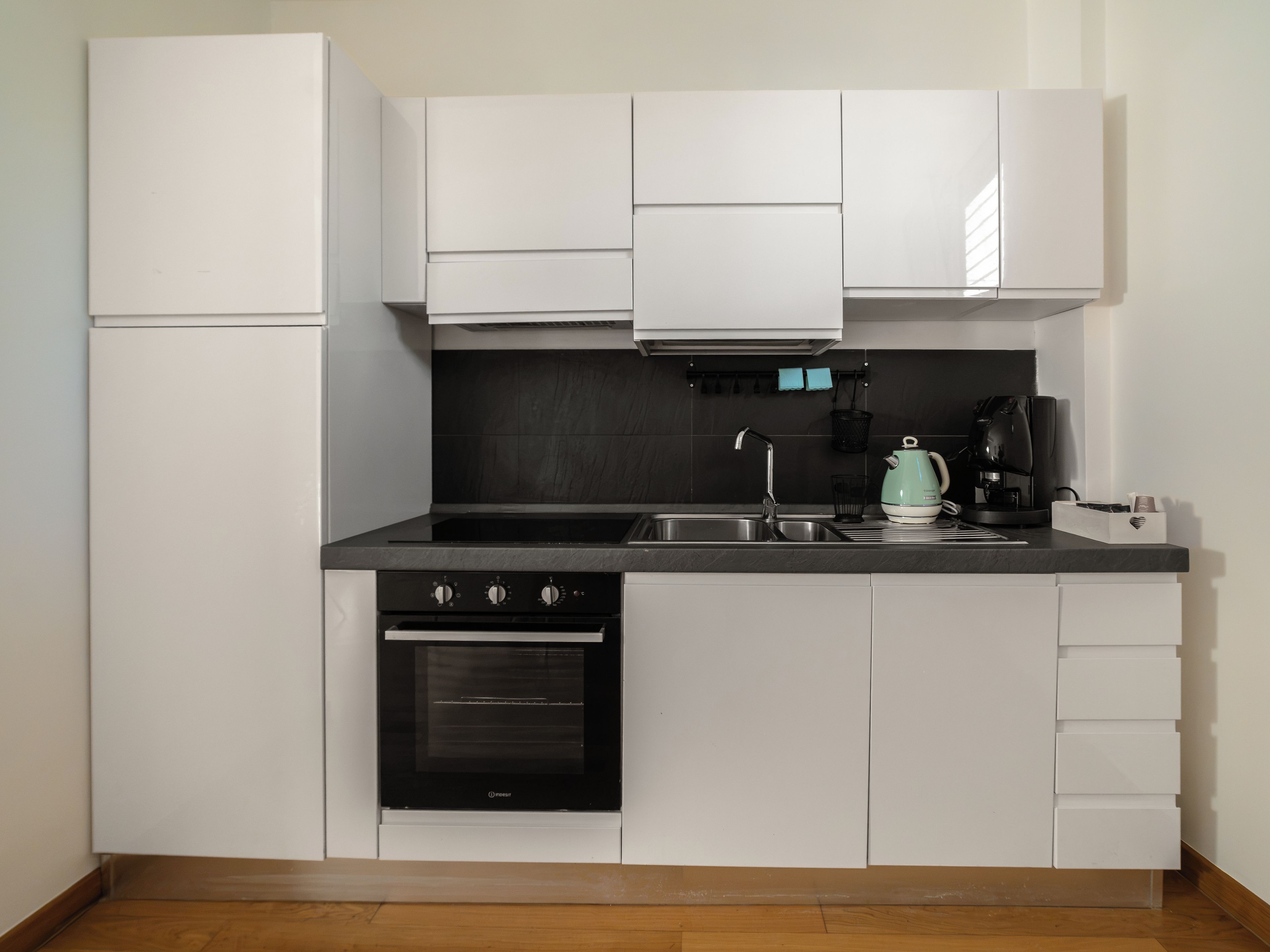 Une cuisine de taille réduite avec des meubles blancs, une cuisinière noire, un évier et une bouilloire.