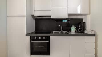 Une cuisine de taille réduite avec des meubles blancs, une cuisinière noire, un évier et une bouilloire.