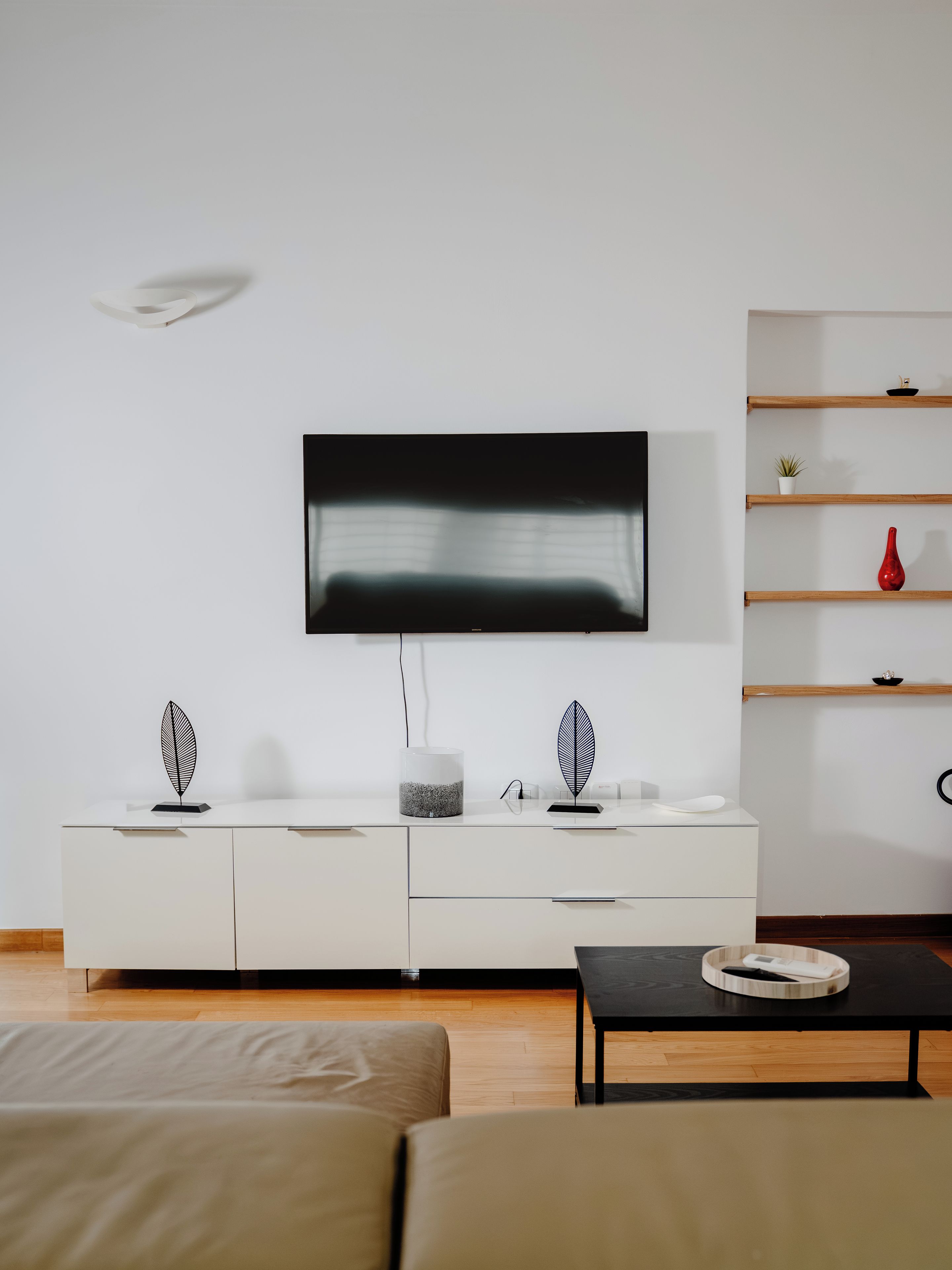 Un salon moderne avec un téléviseur à écran plat fixé au mur, un meuble blanc avec des tiroirs, une table basse noire et un plancher en bois.
