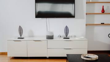 Un salon moderne avec un téléviseur à écran plat fixé au mur, un meuble blanc avec des tiroirs, une table basse noire et un plancher en bois.