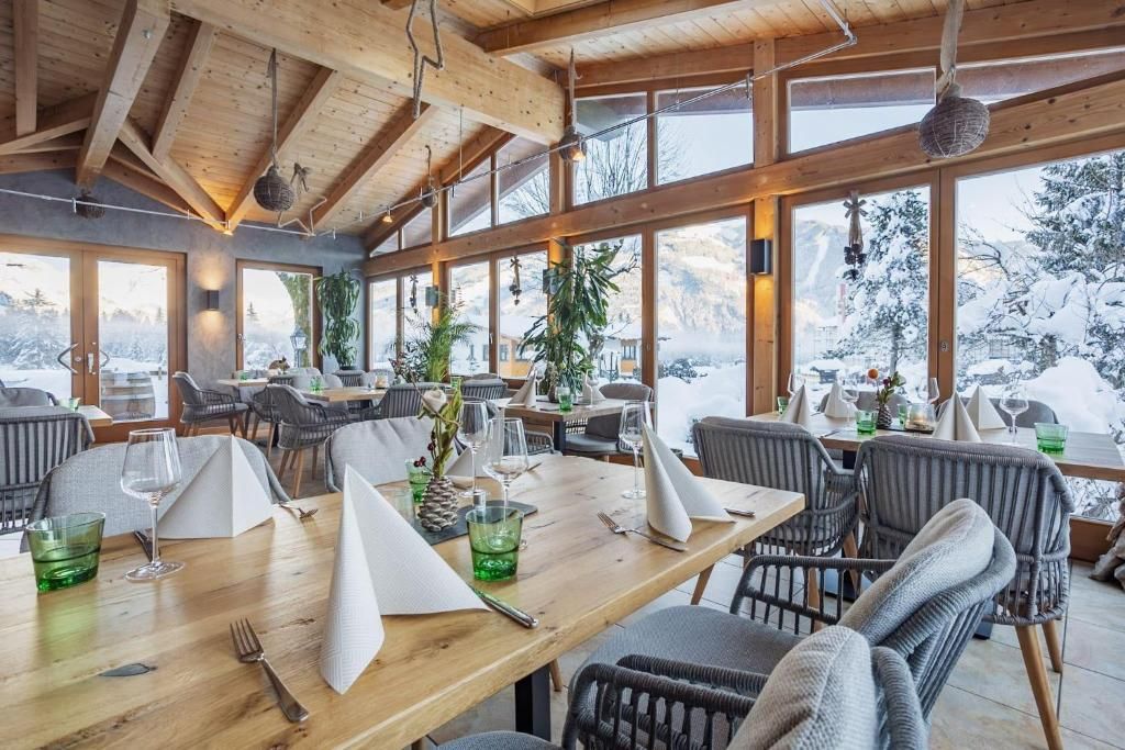Un restaurante con vigas de madera, ventanas amplias y vistas a montañas nevadas.