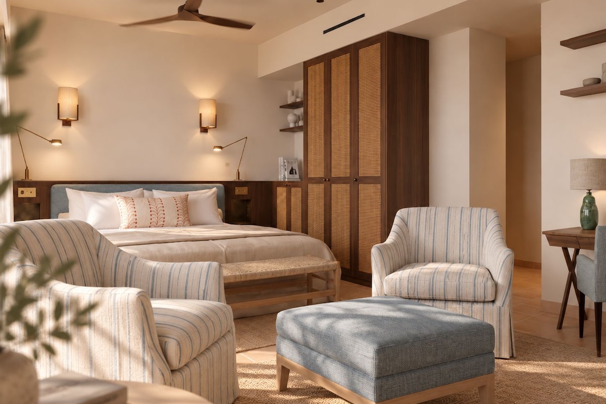 A hotel room with a bed, two armchairs, a sofa, a ceiling fan, and a wall-mounted shelf.