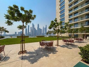 Um pátio com mesas ao ar livre, vista para o horizonte urbano e um edifício com vários andares.