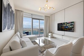 A modern living room with a large window, a flat-screen TV, and a sofa. - Luxury 3BR Palm Views Emaar Beachfront (Dubai)