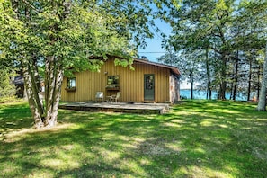 A wooden cabin with a porch, two chairs, and a view of a lake. - Lakefront Home on Deaths Door (Ellison Bay)