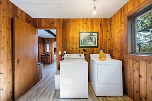 A laundry room with two washing machines, a dryer, and a window with a view of trees. - Lakefront Home on Deaths Door (Ellison Bay)