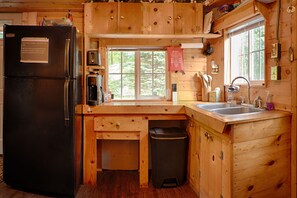 Ett kompakt kök med träskåp, ett svart kylskåp, en diskho och ett fönster som släpper in naturligt ljus.