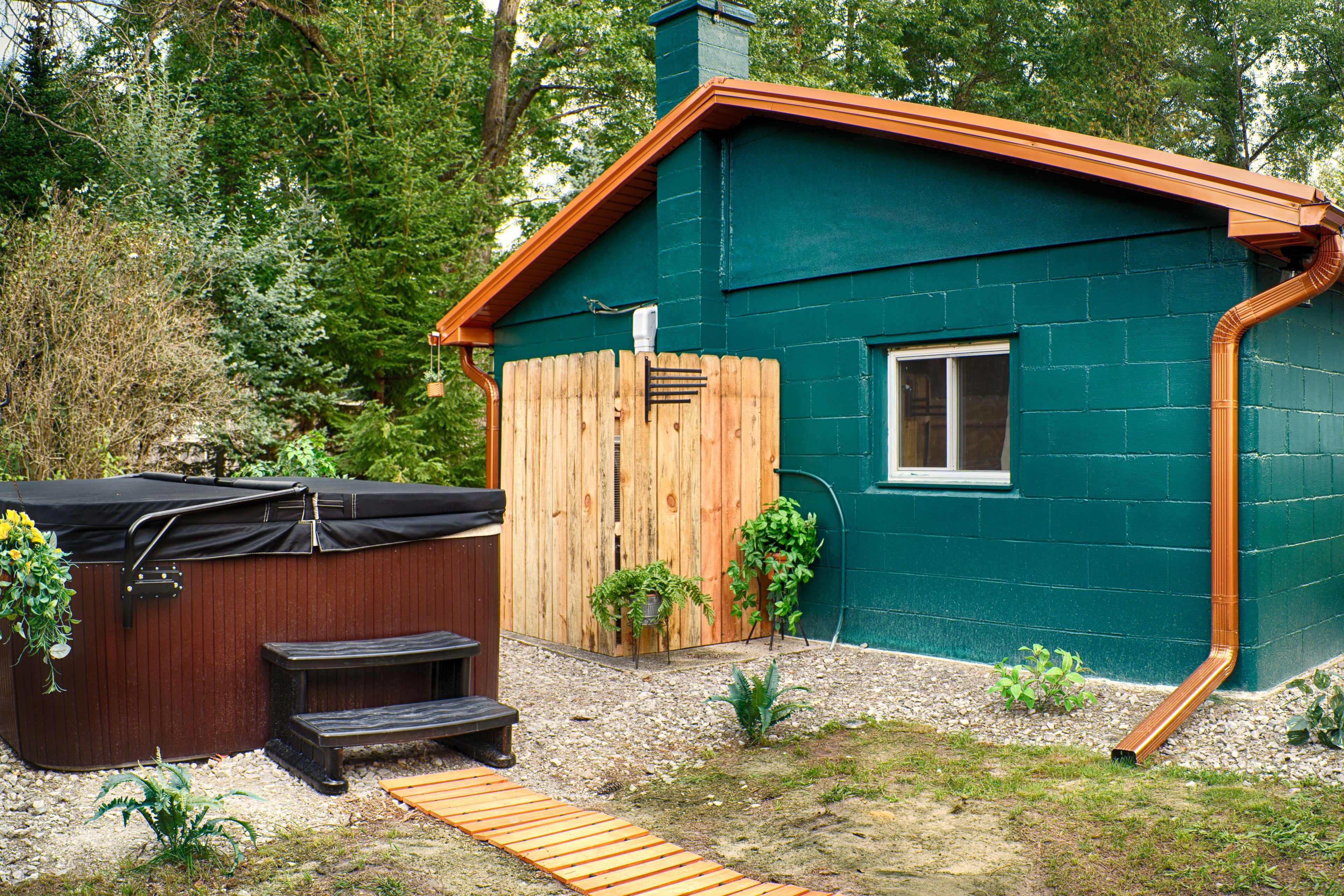 A house with a green exterior, a wooden deck, a hot tub, and a small garden.