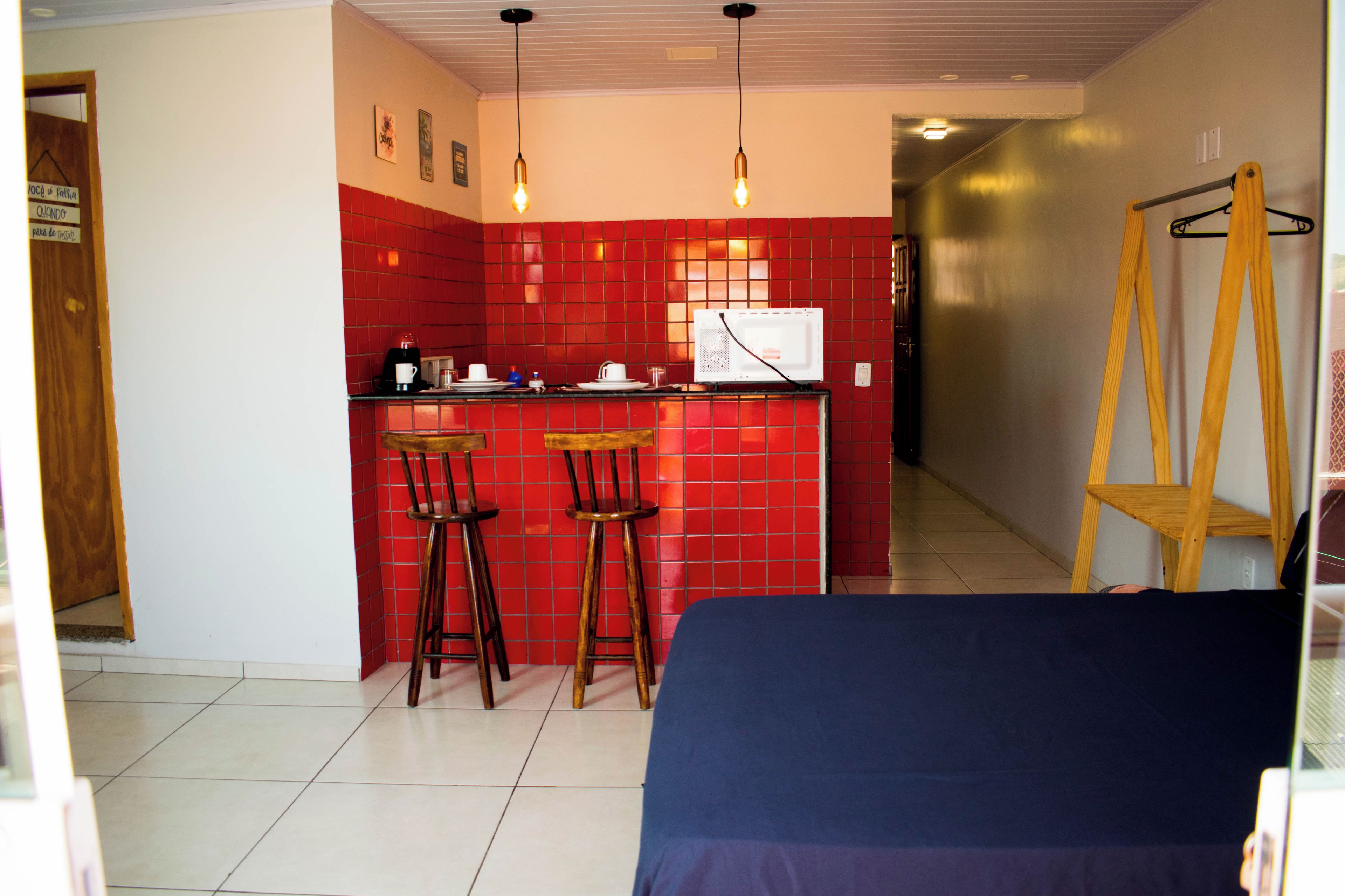 A compact kitchen with red tiles, two bar stools, a microwave, and a coffee maker.