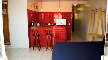 A compact kitchen with red tiles, two bar stools, a microwave, and a coffee maker.