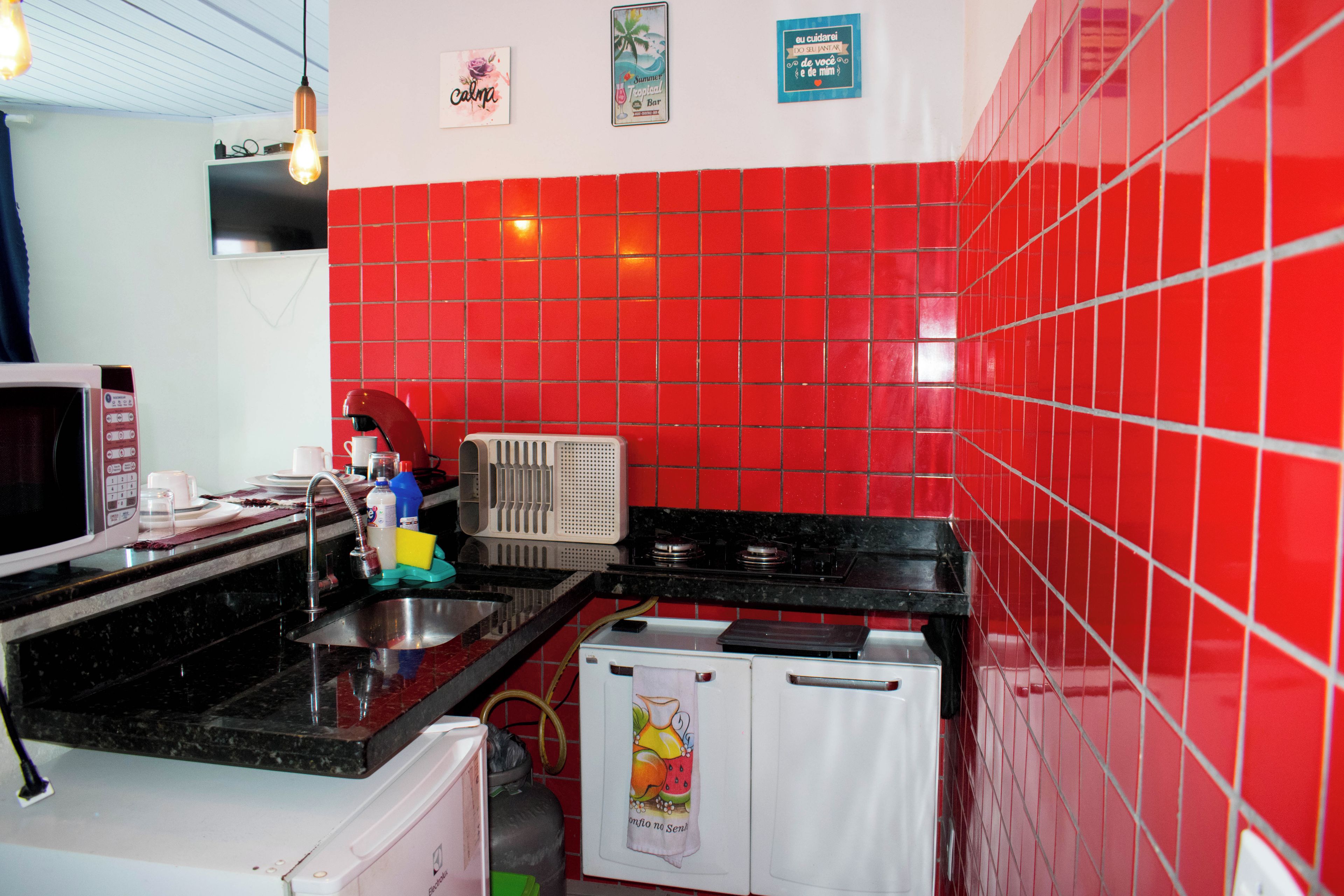 A kitchen with red tiled walls, a microwave, a coffee maker, and a small refrigerator.