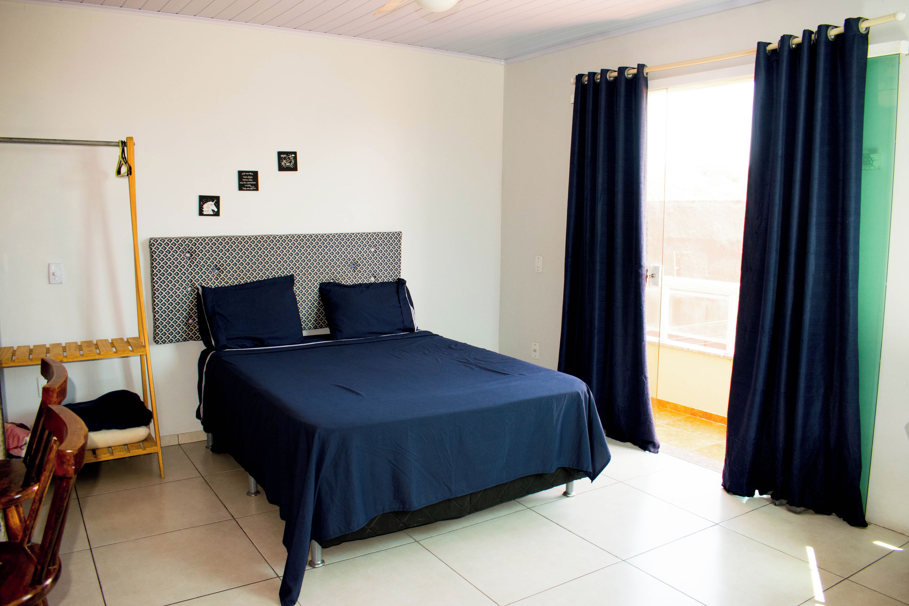 A bedroom with a bed, a wooden chair, a small table, and a window with curtains.