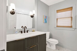 A modern bathroom with a white sink, dark cabinetry, a large mirror, and a toilet. - Pearl Downtown (Mobile)