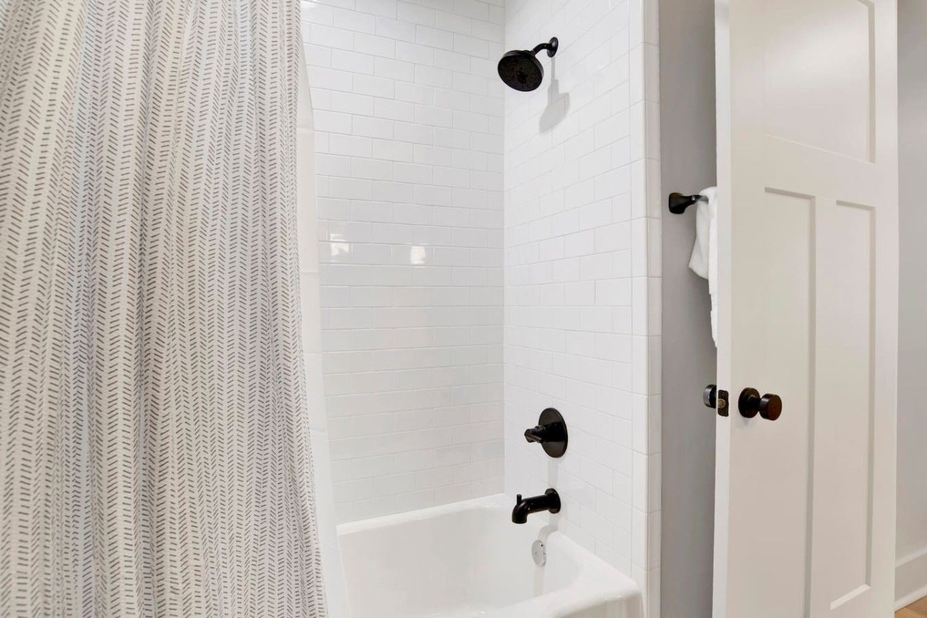 Un baño con ducha, bañera y paredes cubiertas de azulejos blancos.