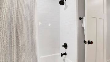 Un baño con ducha, bañera y paredes cubiertas de azulejos blancos.