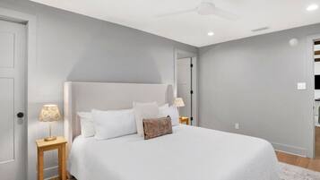 A bedroom with a bed, two bedside tables, a ceiling fan, and a door.