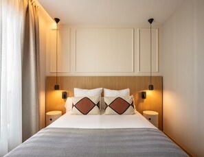 Una habitación de hotel con una cama, dos mesitas de noche, un cabecero y lámparas fijadas a la pared.