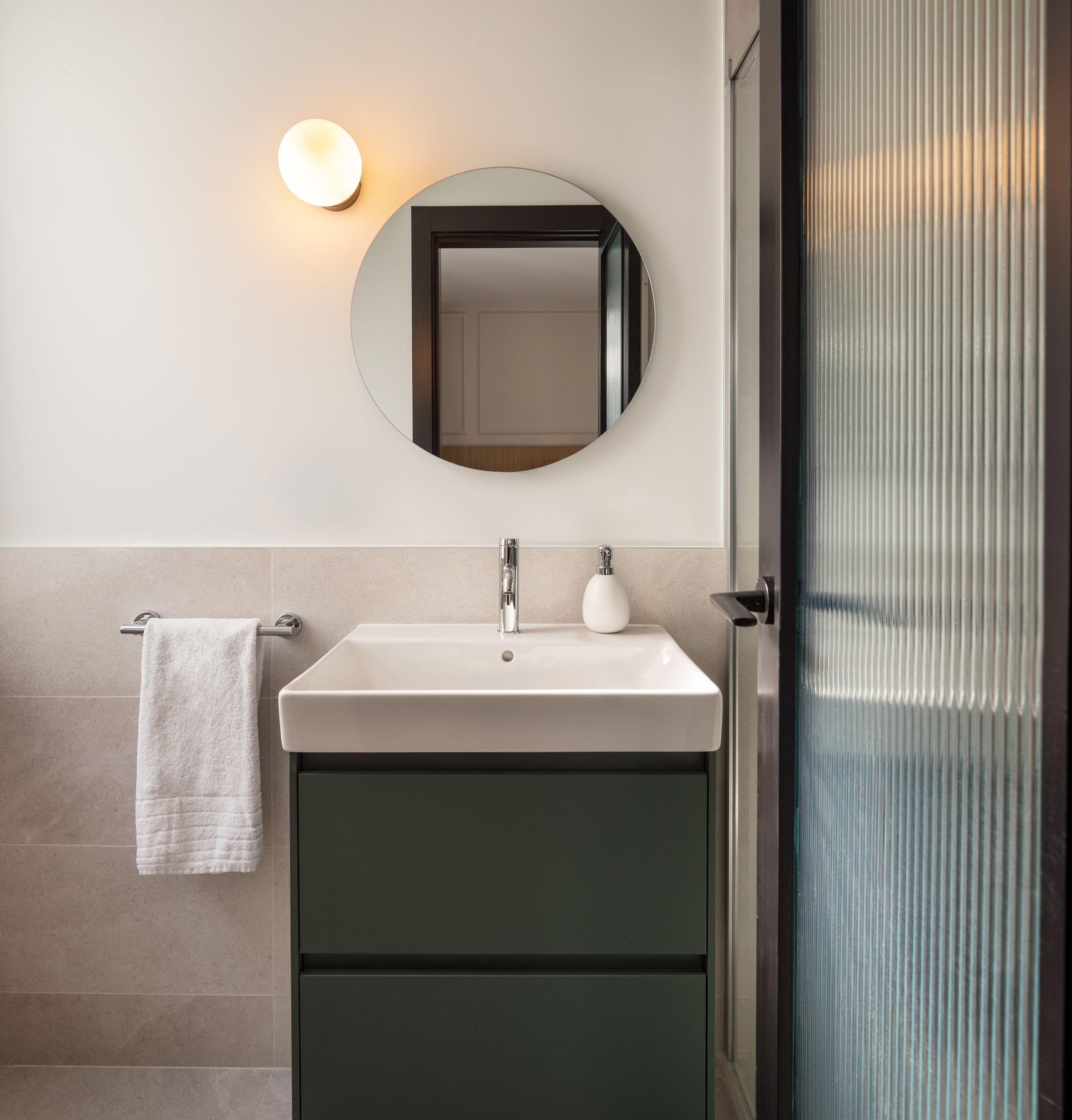 Een badkamer met een wit wastafel, een ronde spiegel en een handdoek aan een rek.