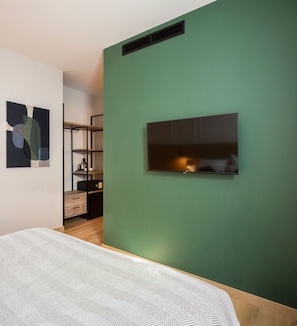 A bedroom with a bed, a TV mounted on the wall, a shelf unit, and a painting on the wall. - Feelathome Las Letras (Madrid)