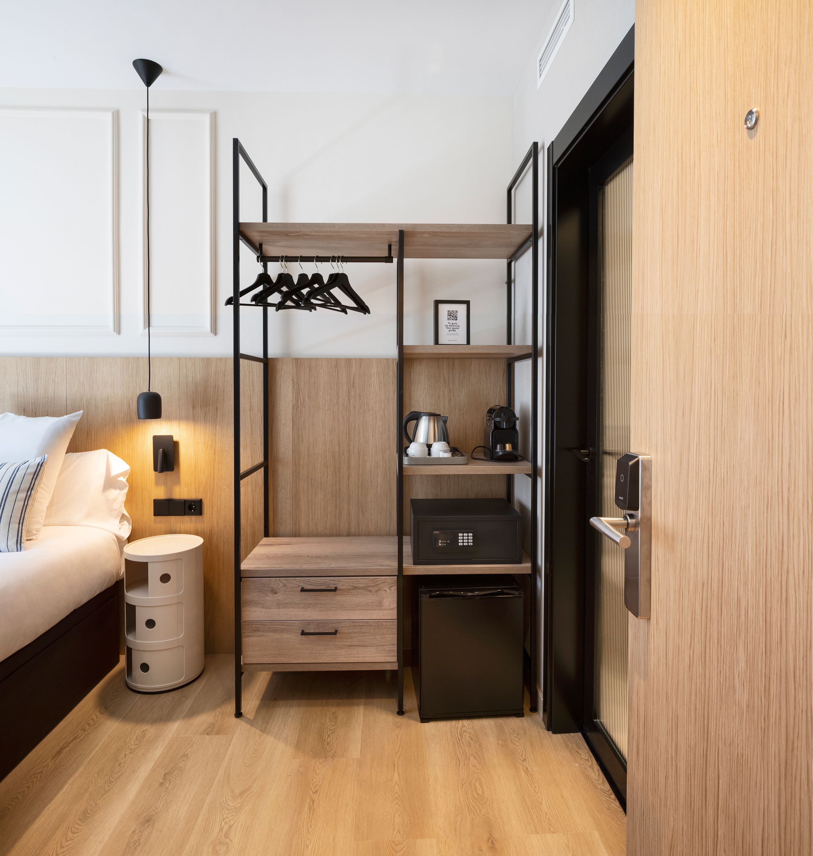 Una habitación pequeña y funcional con cama, mesita de noche, armario y almacenamiento integrado.