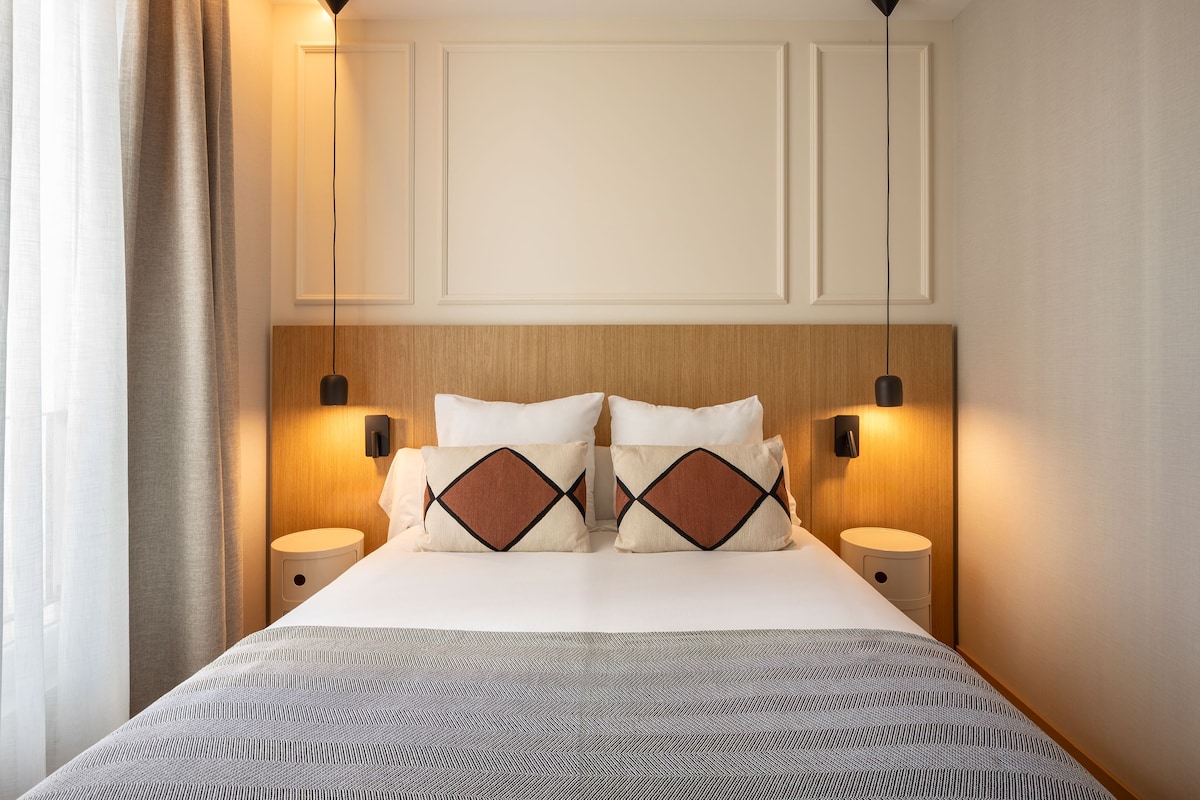 Een hotelkamer met een bed, twee nachtkastjes, een hoofdeinde en wandlampen.